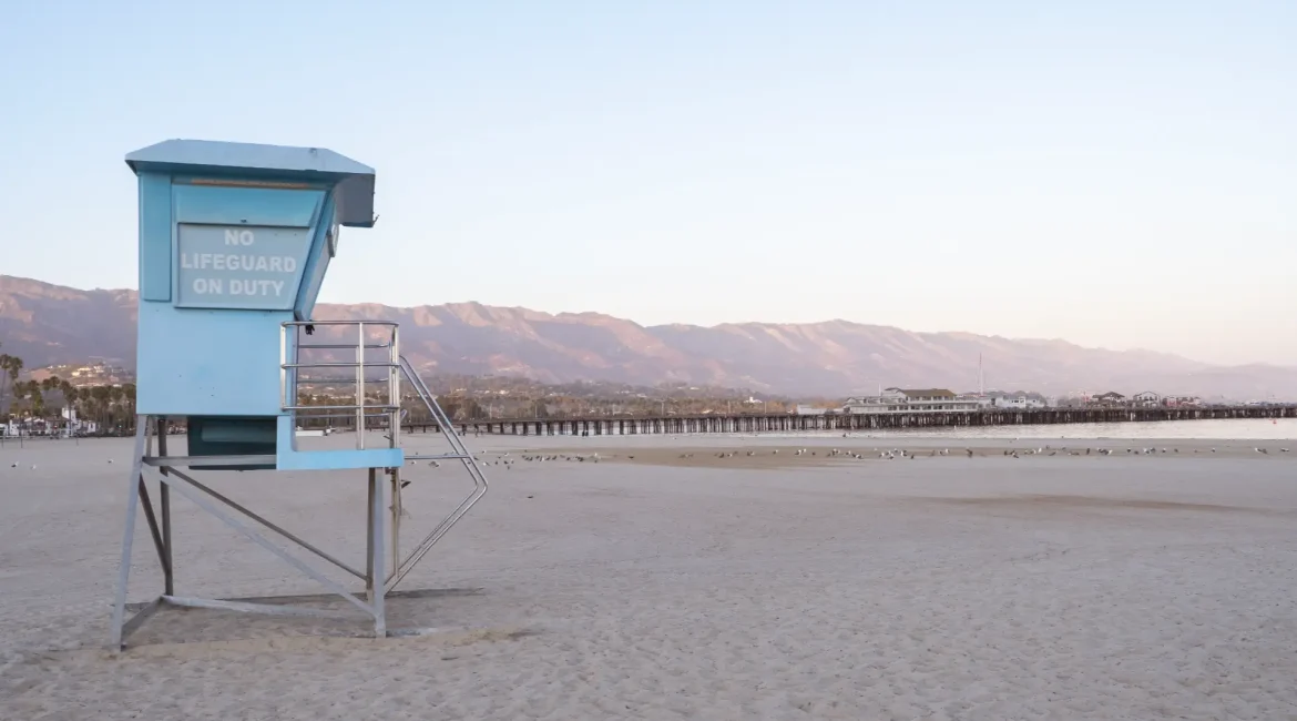 Lifeguard tower on a beach with mountains in the background; two whales visible in the ocean.